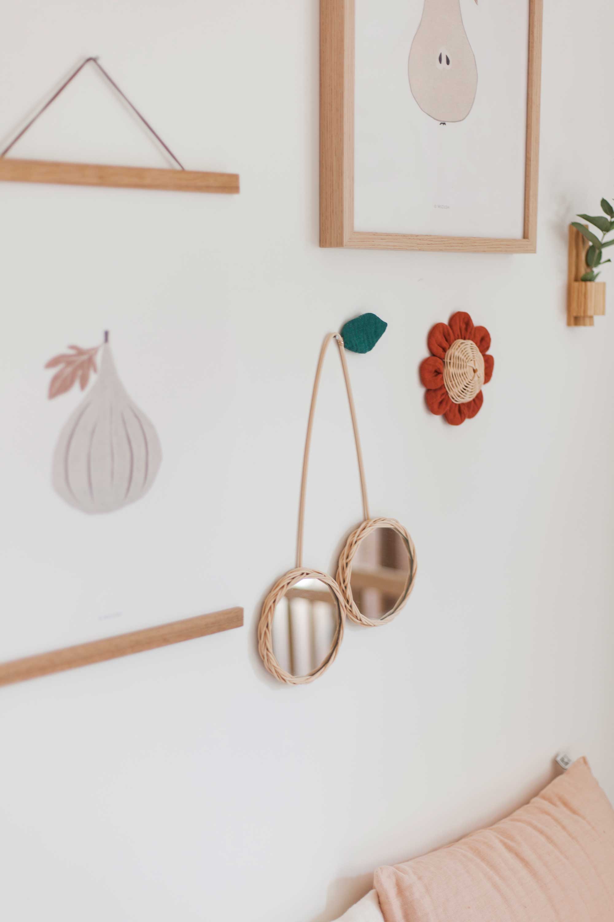 deux produits de la marque atelier solelh sont accrochés au mur. un miroir cerise en rotin et une fleur en rotin. Tous les deux sont réhaussés de tissus colorés.