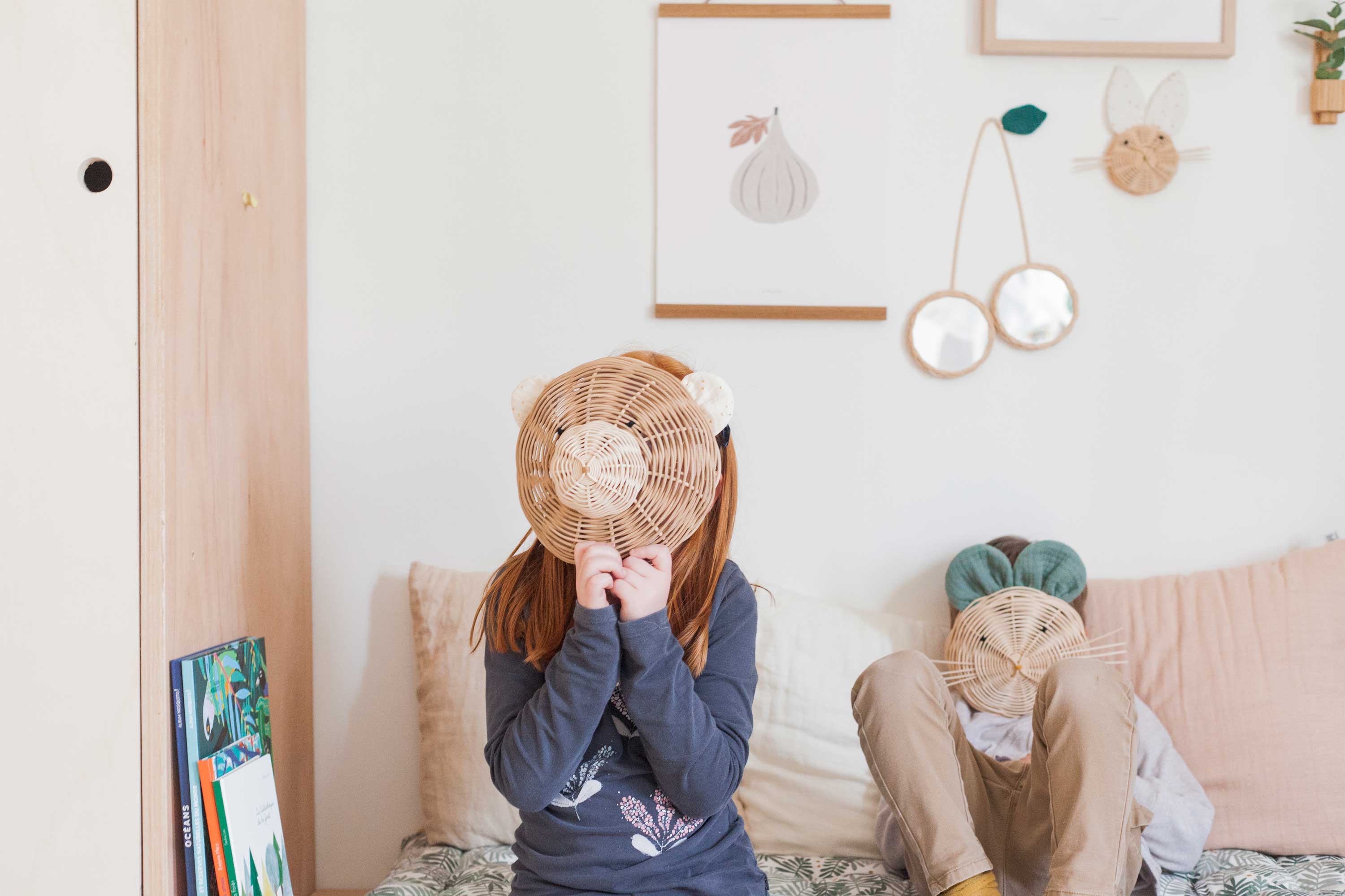 des enfants sont assis sur une banquette et se cachent derrière des trophées en rotin de la marque Atelier Solelh. Un trophée ours et un trophée souris. Sur le mur du fond sont accrochées d'autres produits de la même marque.